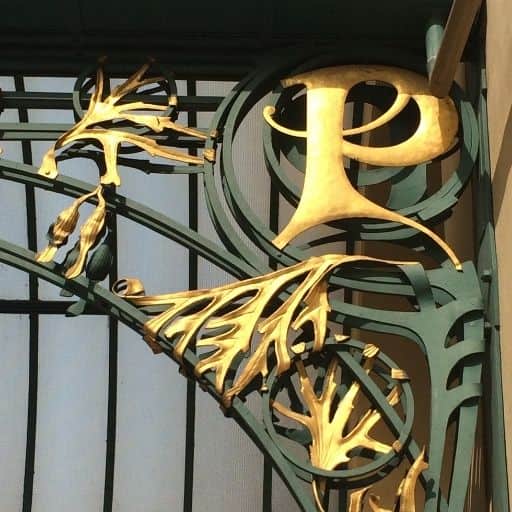Art Nouveau ironwork featuring gilded botanical motifs and a prominent letter P on an Otto Wagner–green archway in Prague.