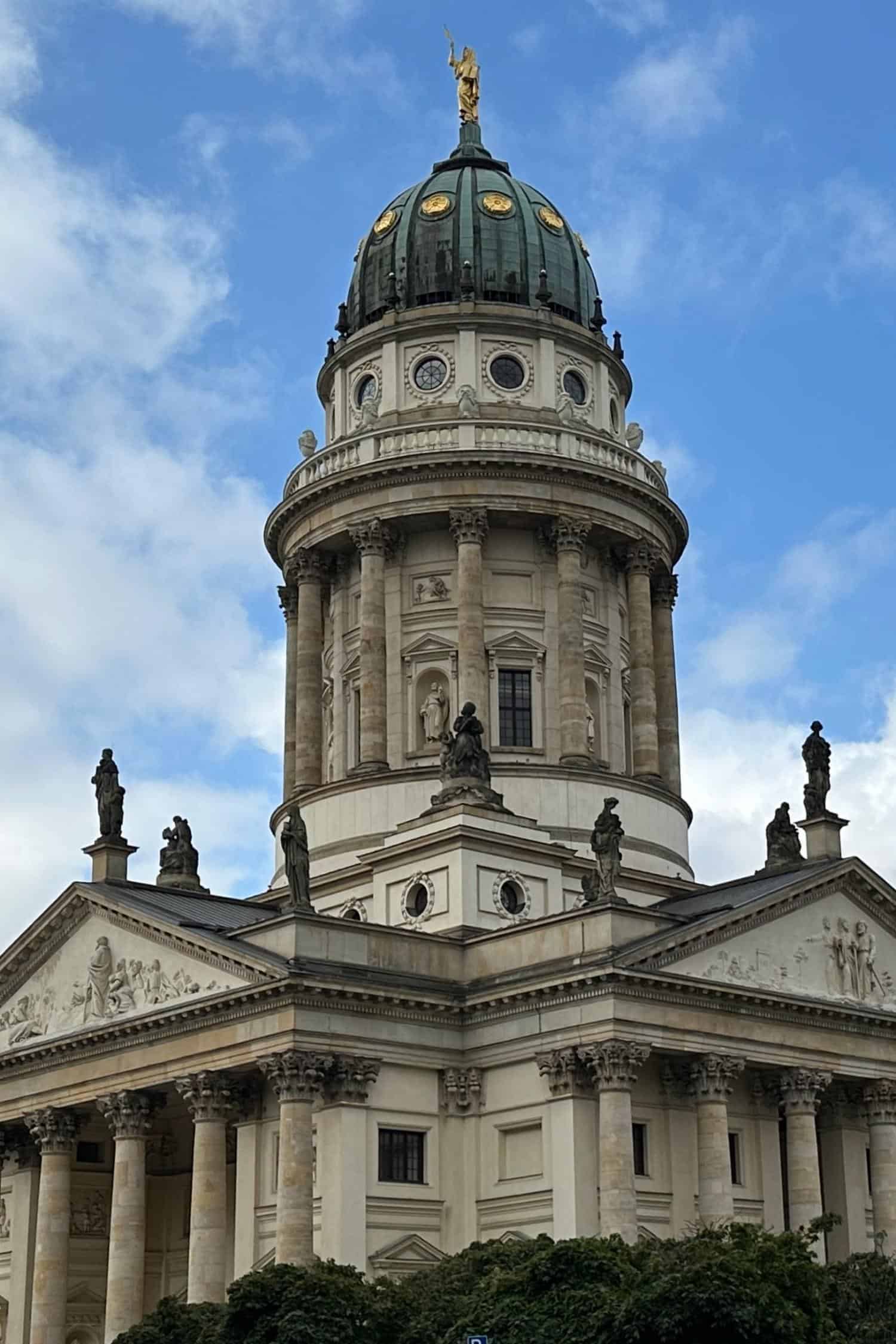 Deutscher Dom at Gendarmenmarkt, Berlin The Deutscher Dom (German Cathedral) on Berlin’s Gendarmenmarkt, showing its domed tower, classical columns, and sculptural pediments against a partly cloudy sky.