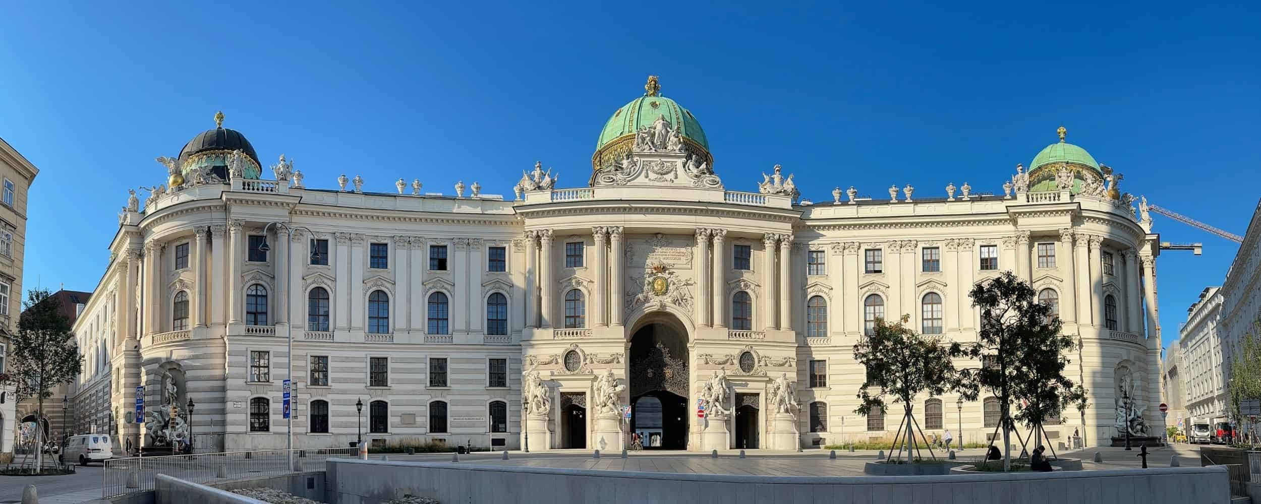 Schönbrunn Palace, Vienna Wide-angle view of Vienna’s Hofburg Palace, highlighting its Baroque façade and central green dome beneath a clear blue sky.