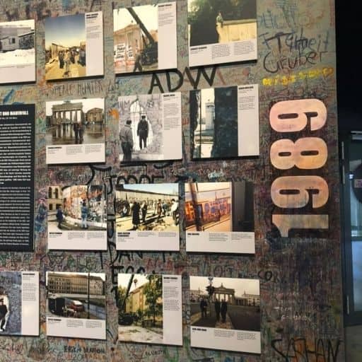 Wall-mounted exhibition installation at the asisi Panorama Die Mauer near Checkpoint Charlie, presenting photographs, documents, and graffiti-style text tracing the full timeline of the Berlin Wall from construction to fall