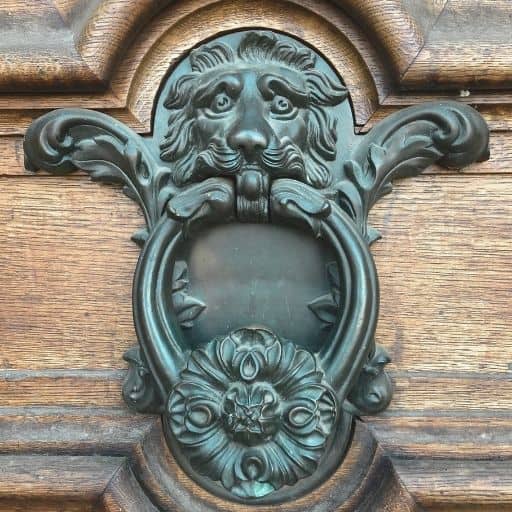 Ornate iron door knocker with a sculpted lion’s head mounted on a carved wooden door in Central Europe.