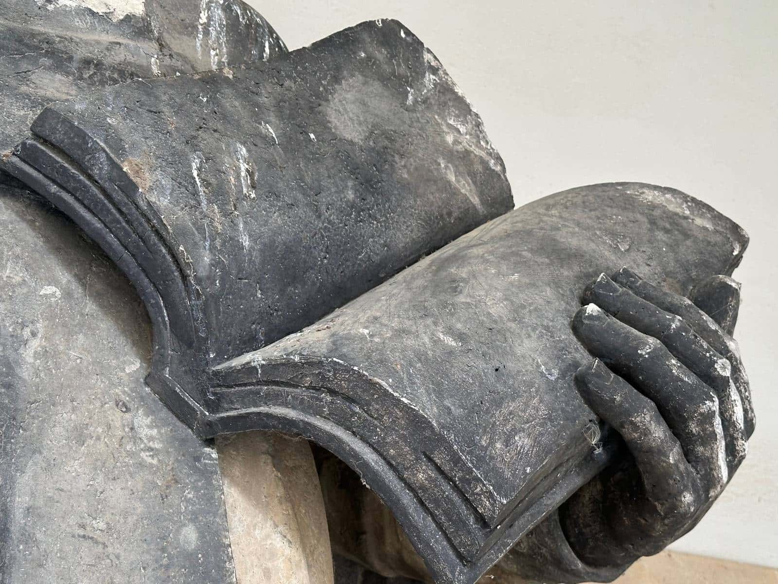Close up of statue with hand holding an open book Stone sculpture detail showing a weathered hand holding an open book, with carved fingers resting gently across the pages