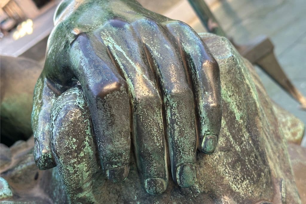 A close-up view of a weathered bronze hand from a statue on the Donner Fountain at Neuer Markt in Vienna.