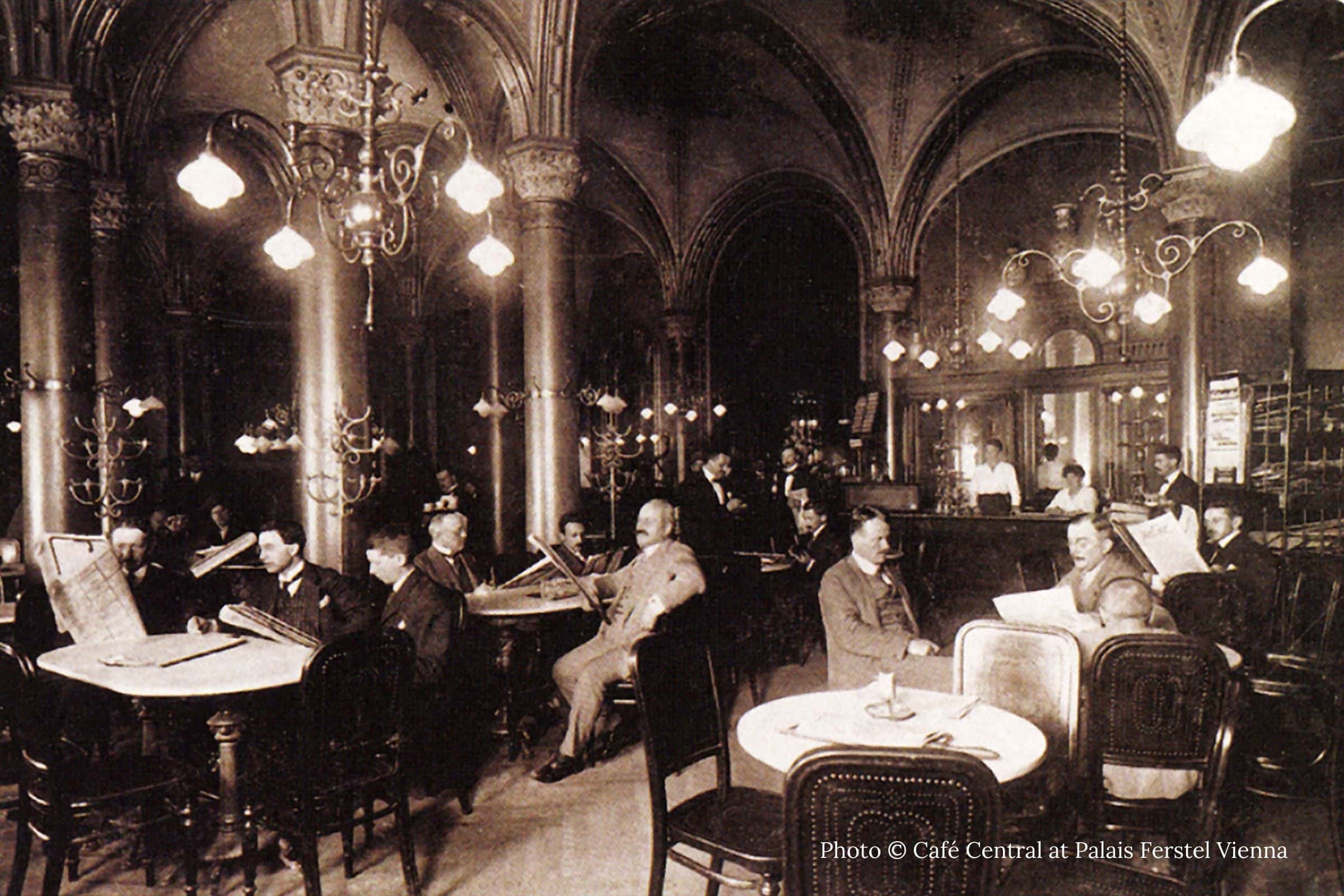 Historic interior of Café Central Vienna with vaulted ceilings gaslight chandeliers and patrons reading newspapers