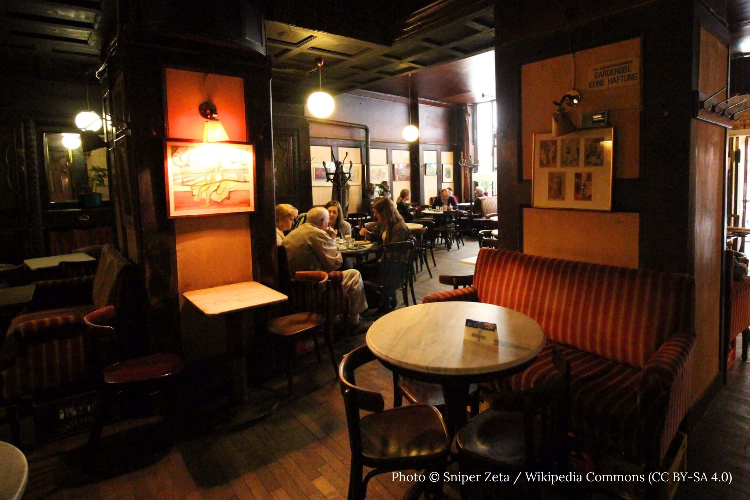 Interior of Café Hawelka Vienna with dark wood paneling marble tables and patrons seated beneath globe lights