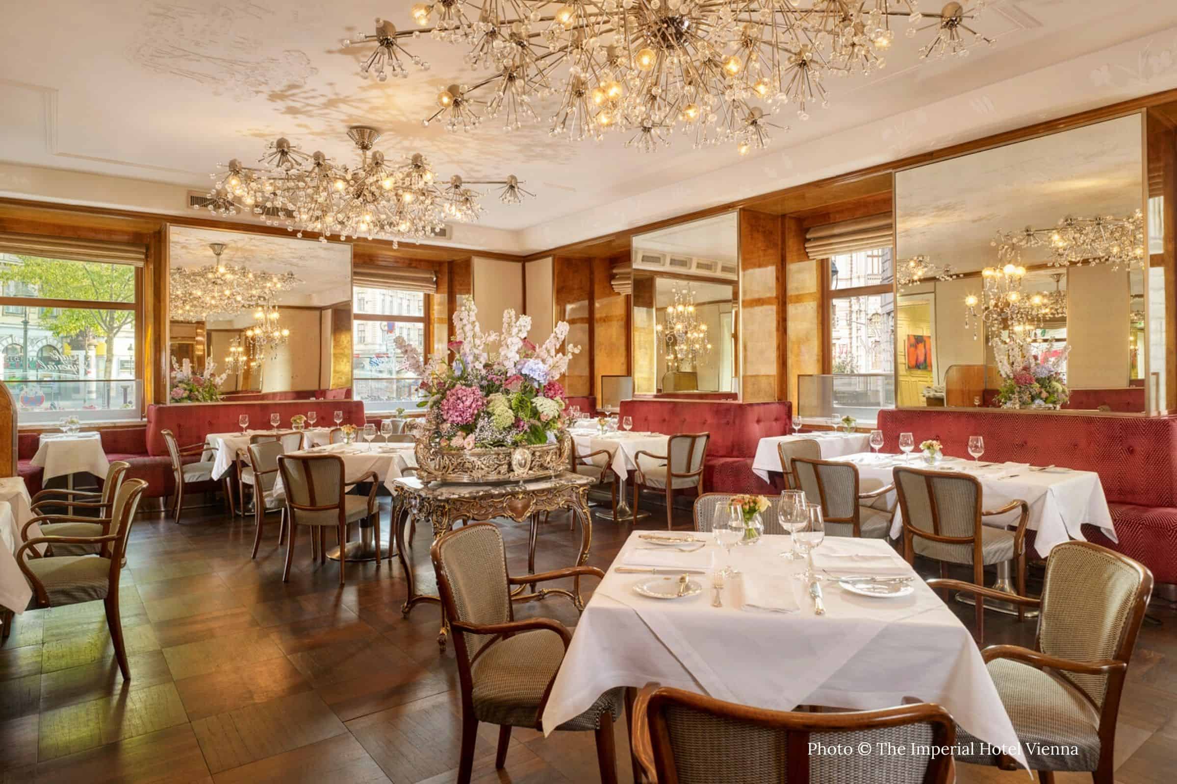 Café Imperial Vienna dining room with crystal chandeliers Café Imperial dining room in Vienna with crystal starburst chandeliers, mirrored walls, and white-linen tables