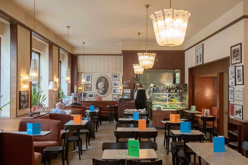 Café Korb interior in Vienna with marble tables, upholstered banquettes, hanging glass chandeliers, and pastry counter