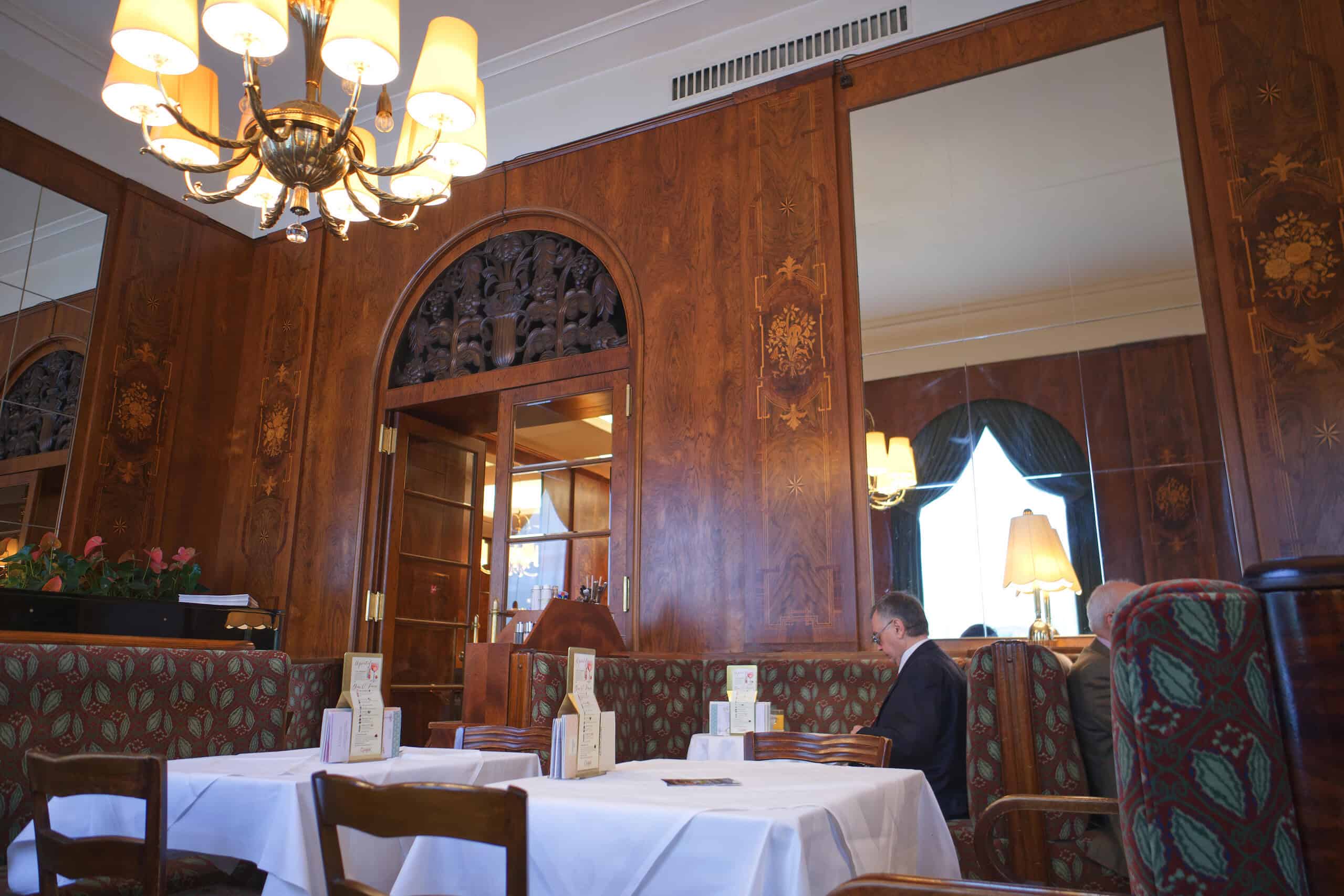 Café Landtmann, Vienna — historic coffeehouse interior Café Landtmann interior with wood-paneled walls, chandeliers, upholstered banquettes, and white tablecloths