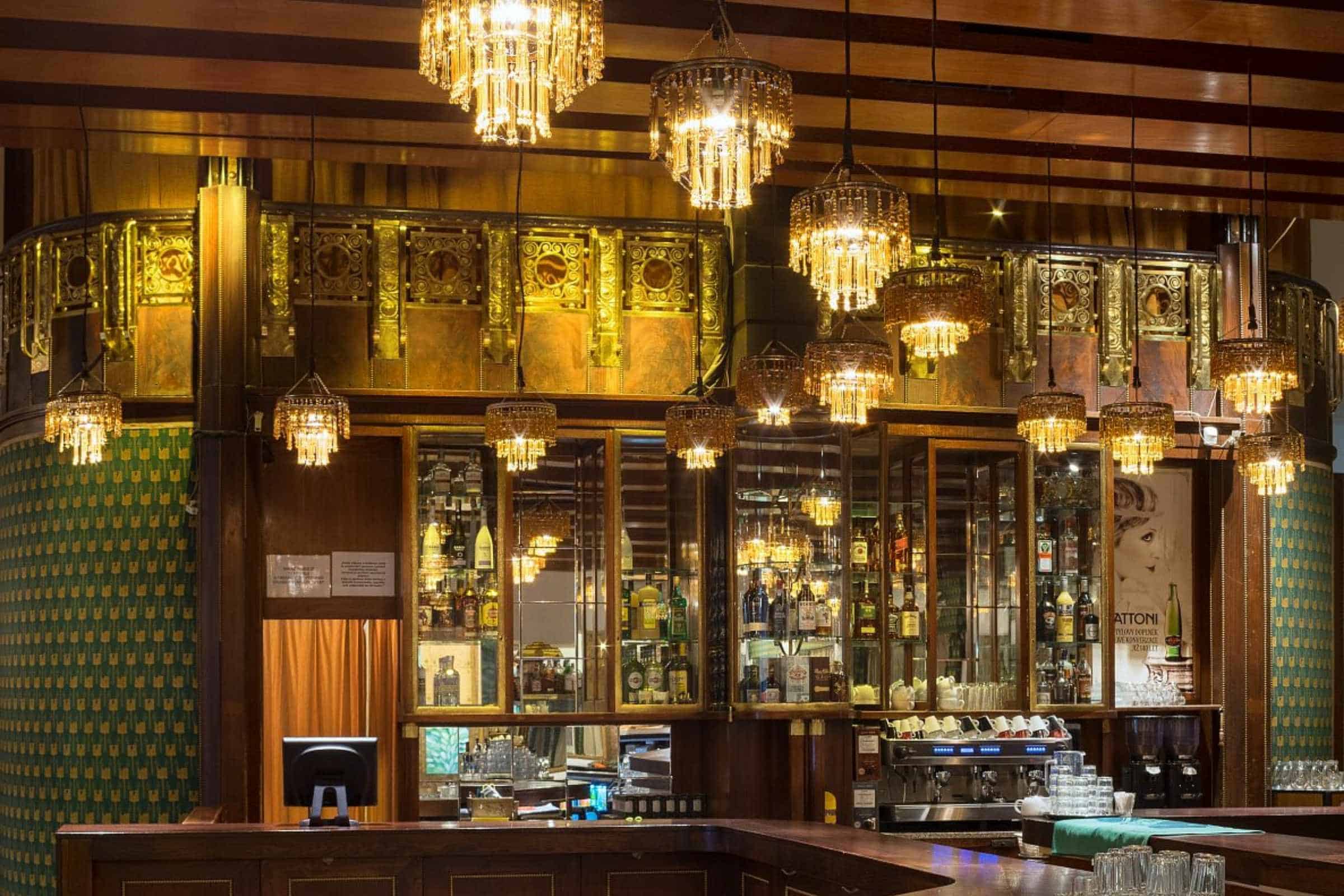 Art Deco bar interior at Café Lucerna in Prague with gilded woodwork, mirrored shelves, and cascading crystal chandeliers