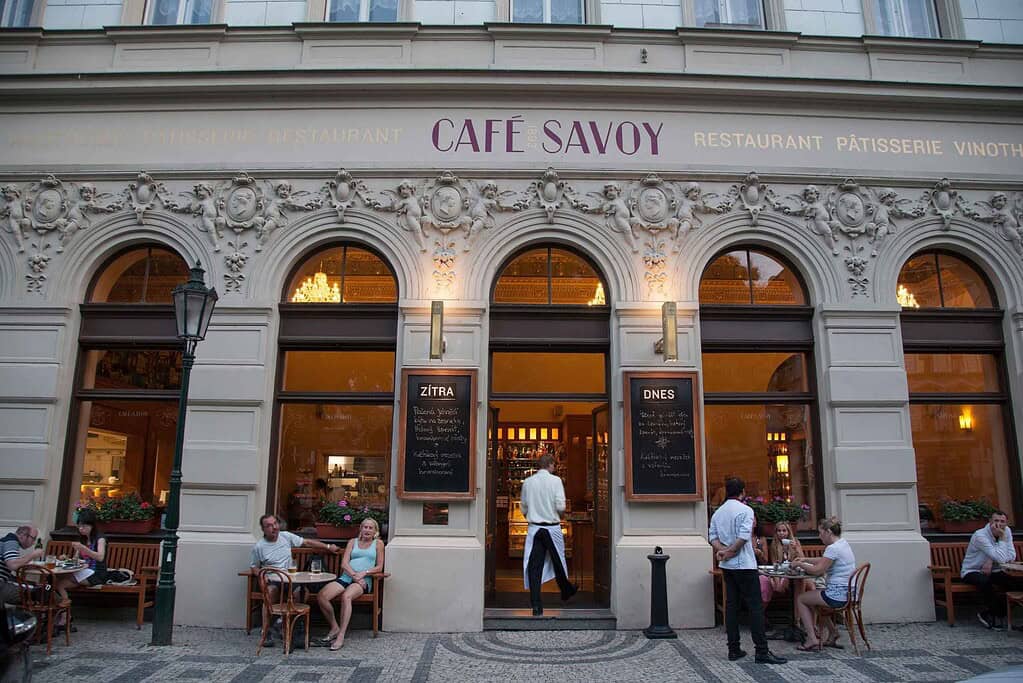 Exterior of Café Savoy in Prague with arched windows, decorative stucco façade, and patrons seated at outdoor tables