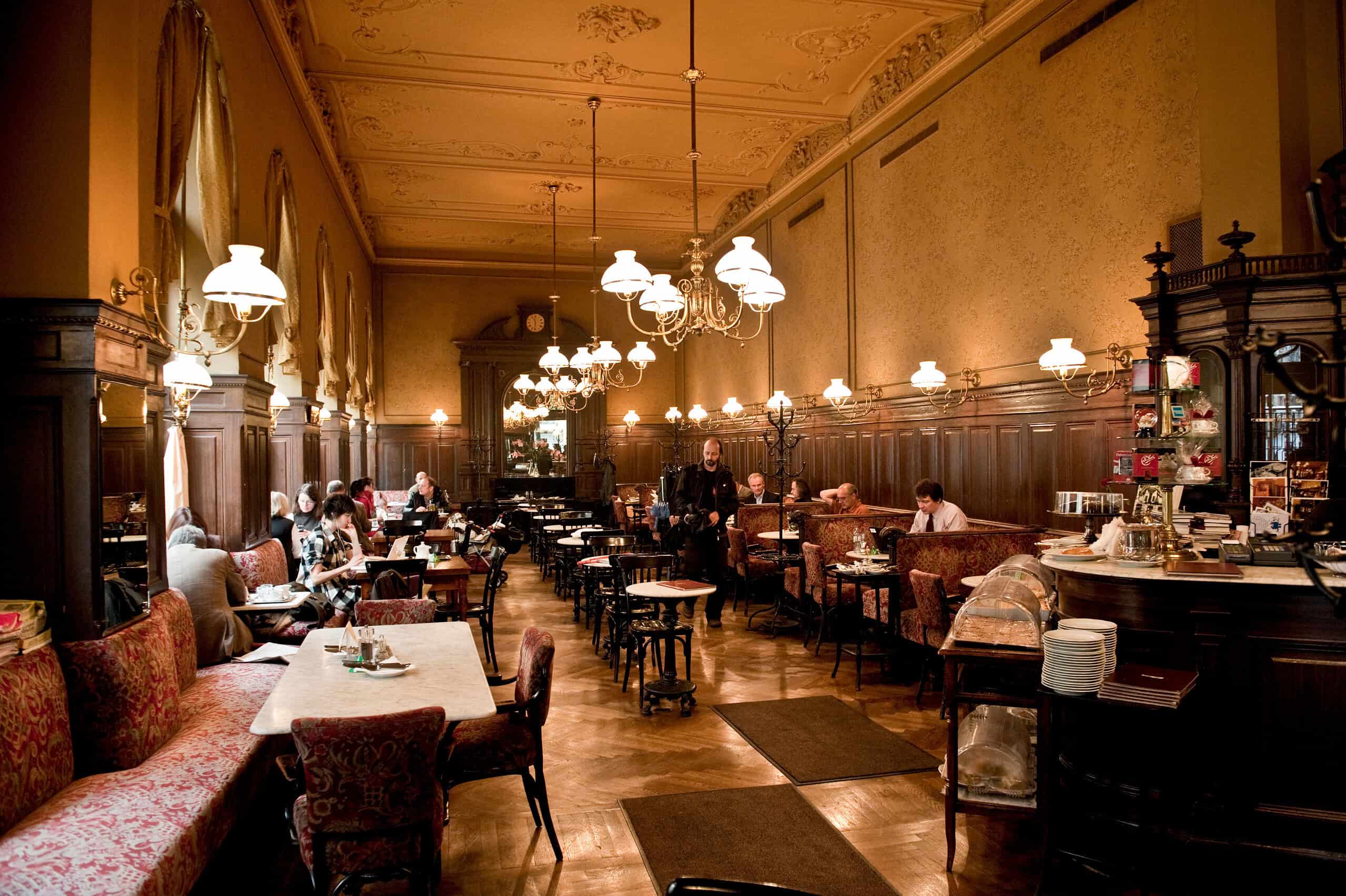 Café Sperl interior in Vienna with long wood-paneled hall, marble tables, chandeliers, and seated patrons