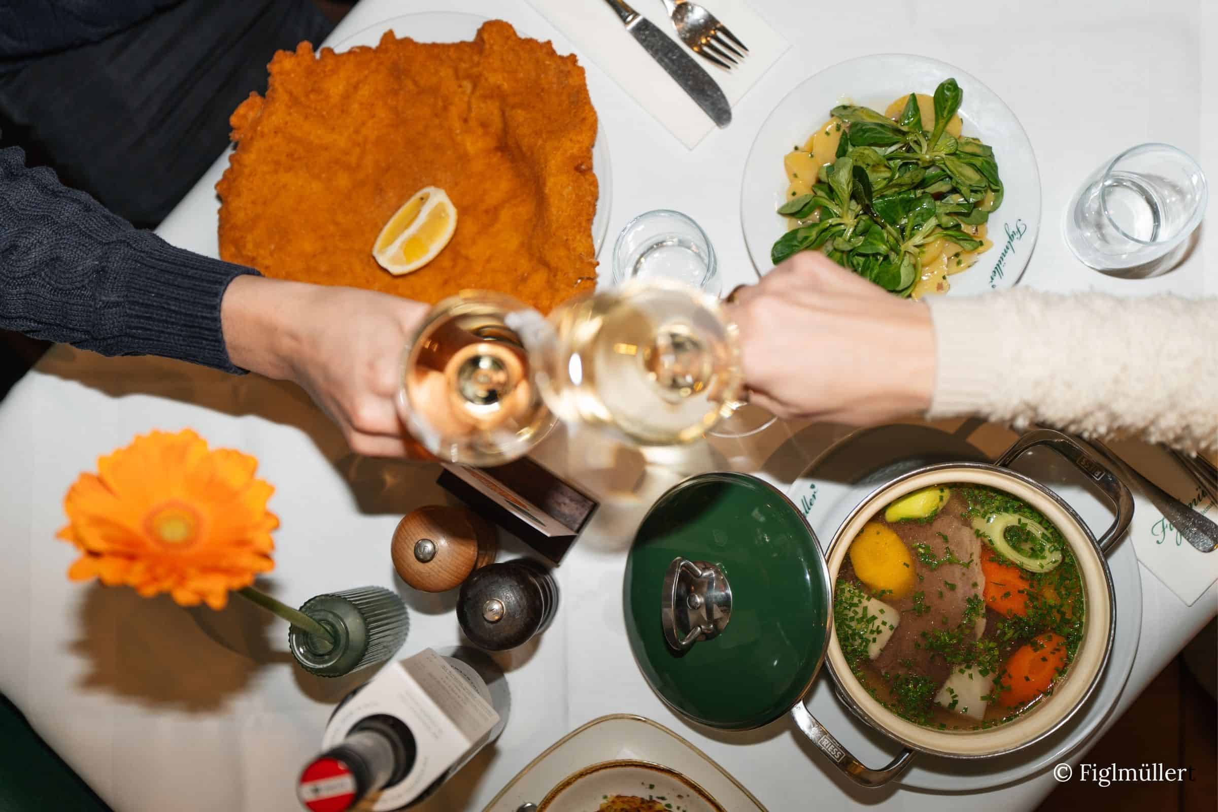 Wiener Schnitzel and wine at Figlmüller, Vienna Overhead view of a Wiener Schnitzel meal at Figlmüller with potato salad, broth, and glasses of wine being toasted
