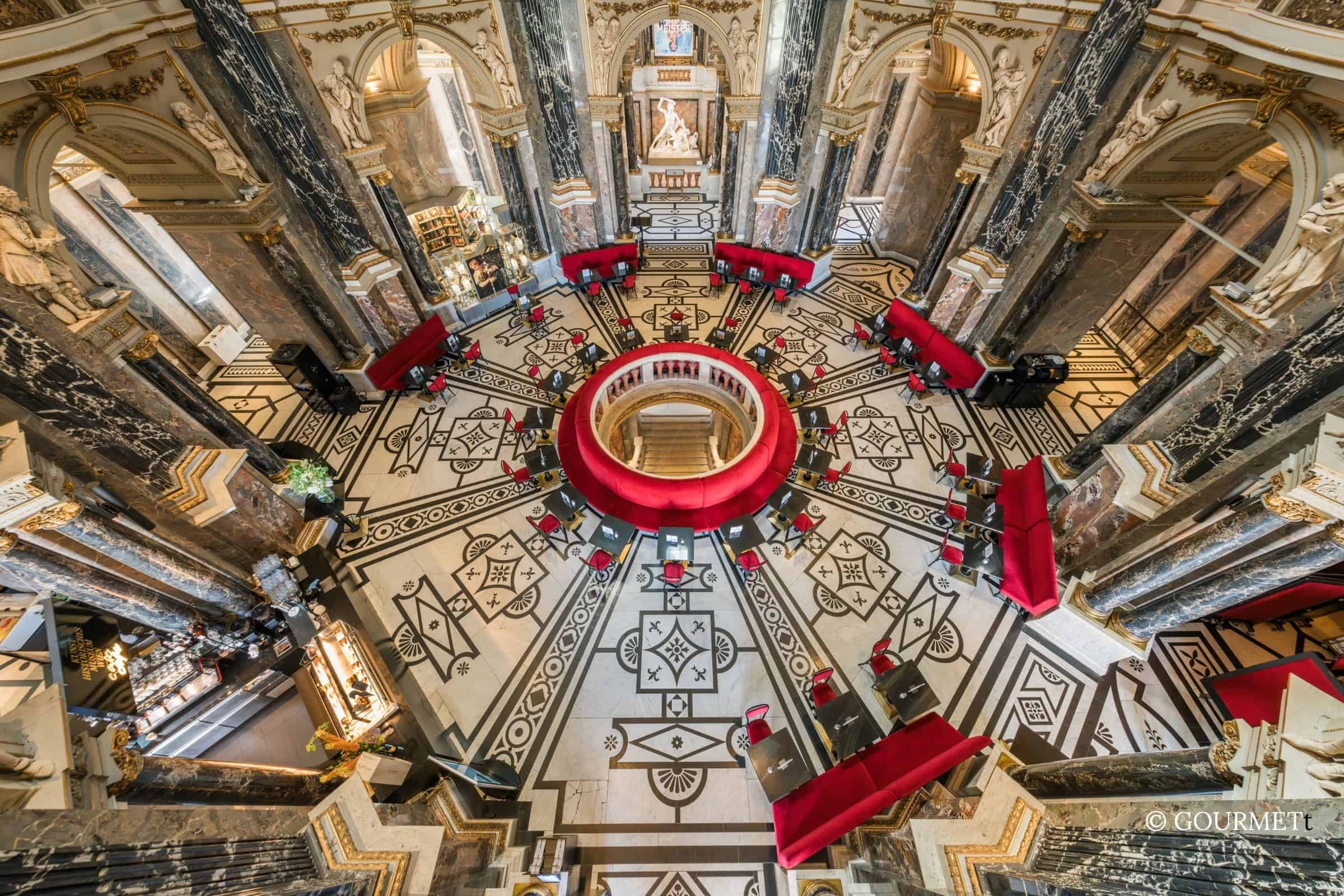 Kunsthistorisches Museum Café interior with marble floor and circular seating Overhead view of the Kunsthistorisches Museum café in Vienna, featuring a circular red banquette, patterned marble floor, and grand historic architecture