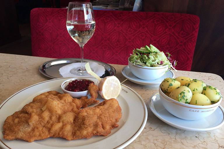Wiener schnitzel served at Café Museum in Vienna, accompanied by parsley potatoes, green salad, lingonberry sauce, lemon, and a glass of white wine