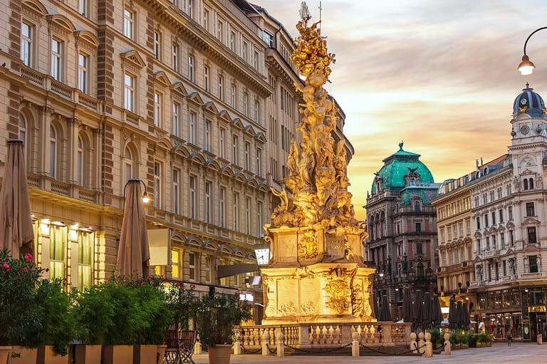 The illuminated Baroque Plague Column (Pestsäule) on Vienna’s Graben at dusk, surrounded by historic buildings beneath a golden evening sky