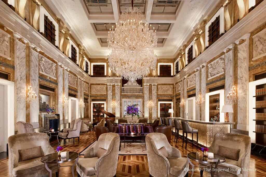 Exterior and interior views of Hotel Imperial Vienna on the Ringstraße, including its illuminated palace façade, grand marble lobby bar with chandelier, and green and gold junior suite