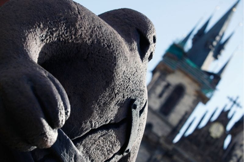 Statue of the Prague Golem in Old Town with the Gothic spires of the Church of Our Lady before Týn rising in the background