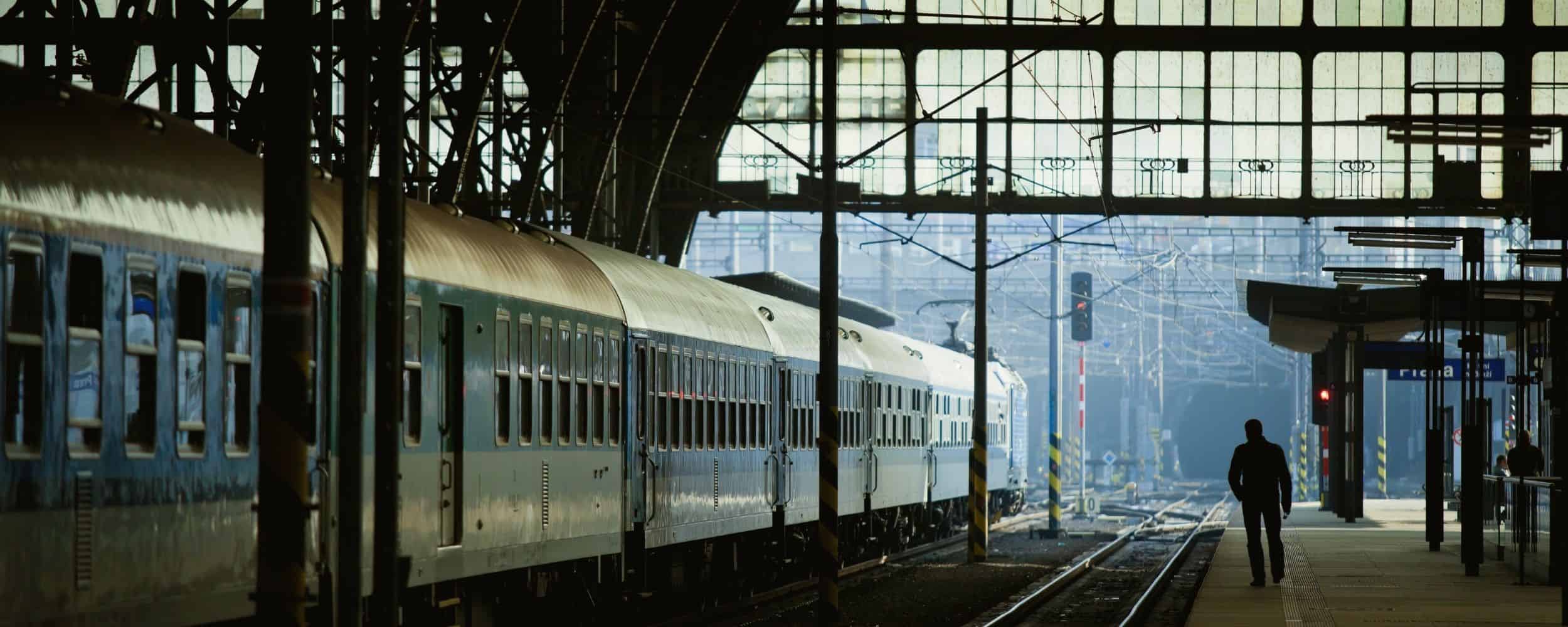 Silhouetted traveler walking beside a passenger train at Prague’s main railway station