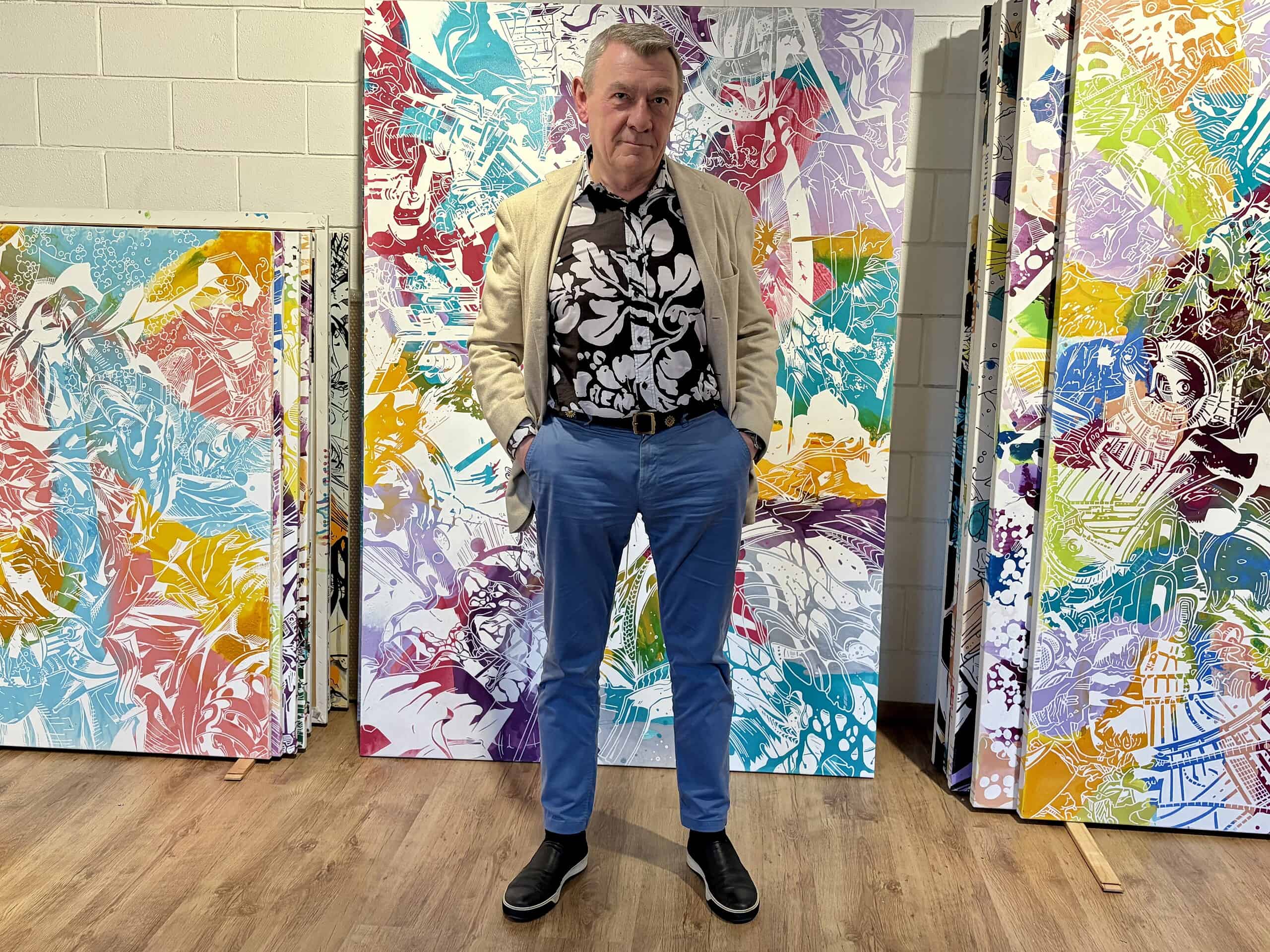 Herwig Kempinger posing in front of his brightly colored abstract art.
