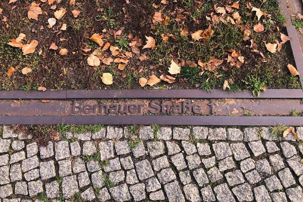 Berlin Wall marker on Bernauer Straße surrounded by fallen autumn leaves and cobblestones