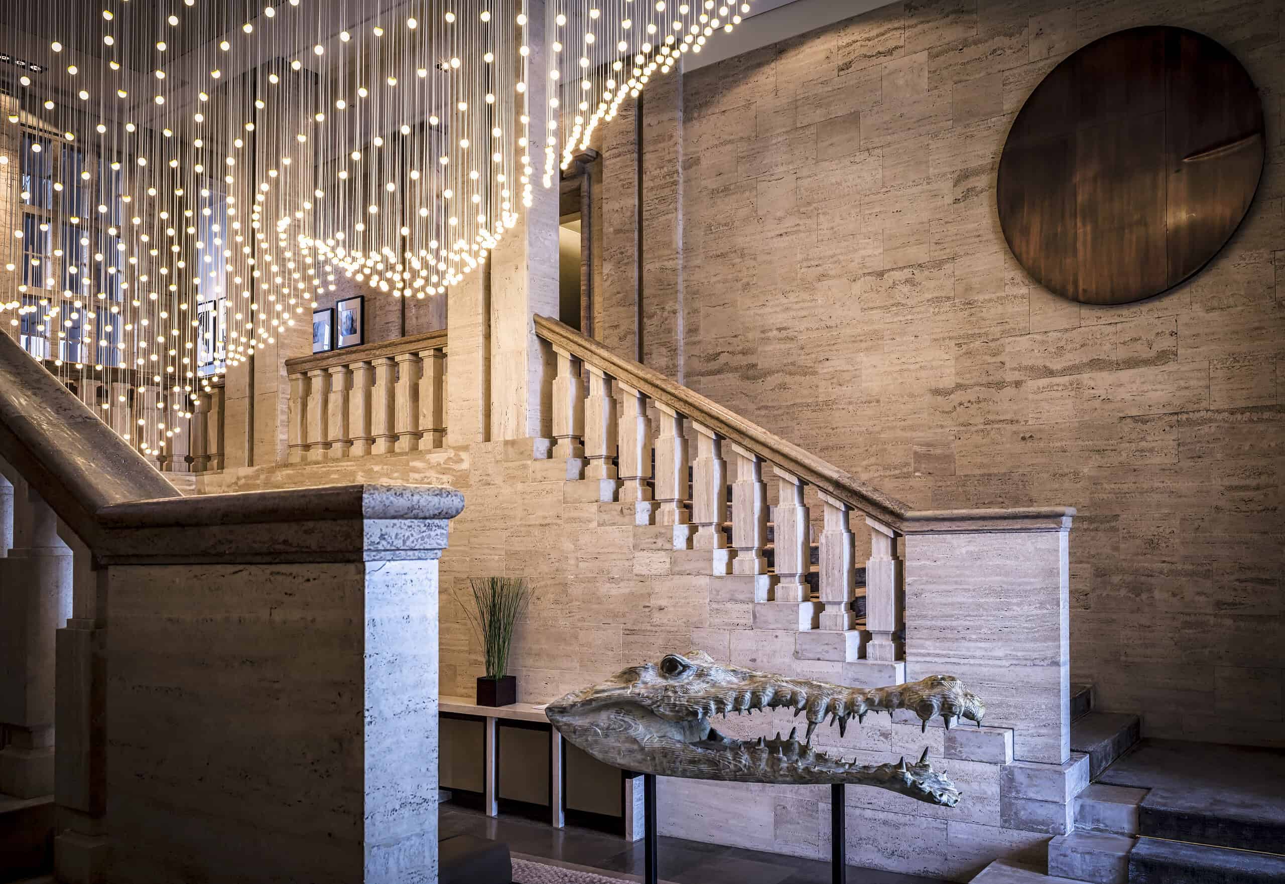 Lobby at Das Stue Berlin with stone staircase, contemporary lighting installation, and crocodile sculpture