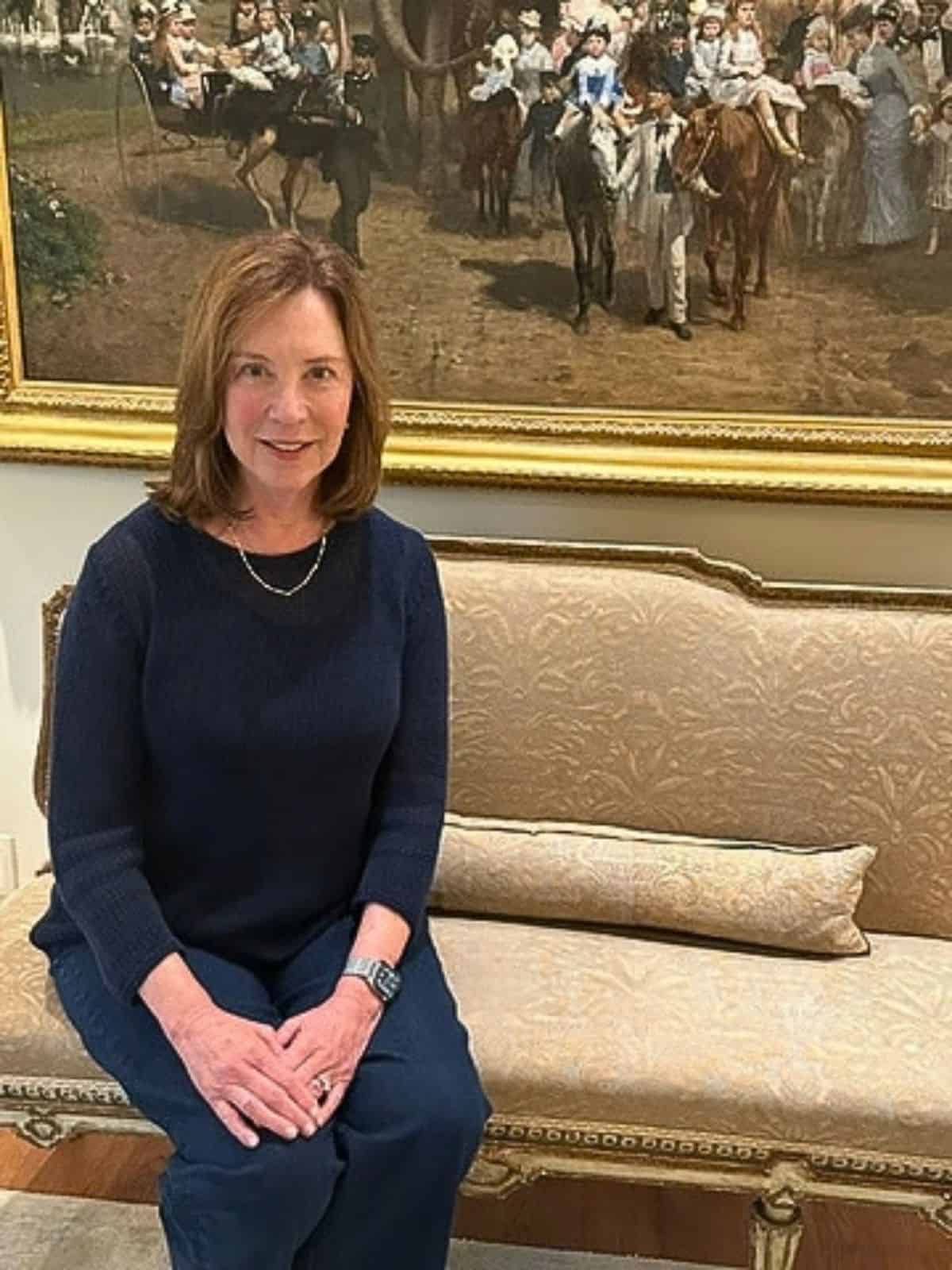 Guest Columnist Donna Eacho seated beneath Otto von Thoren’s painting “Afternoon at the Zoo, Bois de Vincennes, Paris” during an interview for The Triptych Unpacked