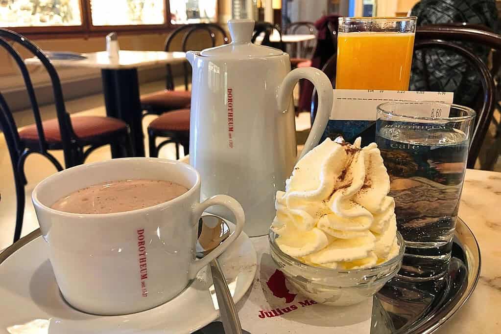 A pot of hot chocolate with a side of fresh cream and a glass of water served on a silver tray at a Viennese cafe
