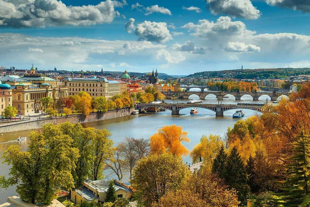 Panoramic view of Prague in autumn with the Vltava River, Charles Bridge, historic rooftops, and golden fall foliage