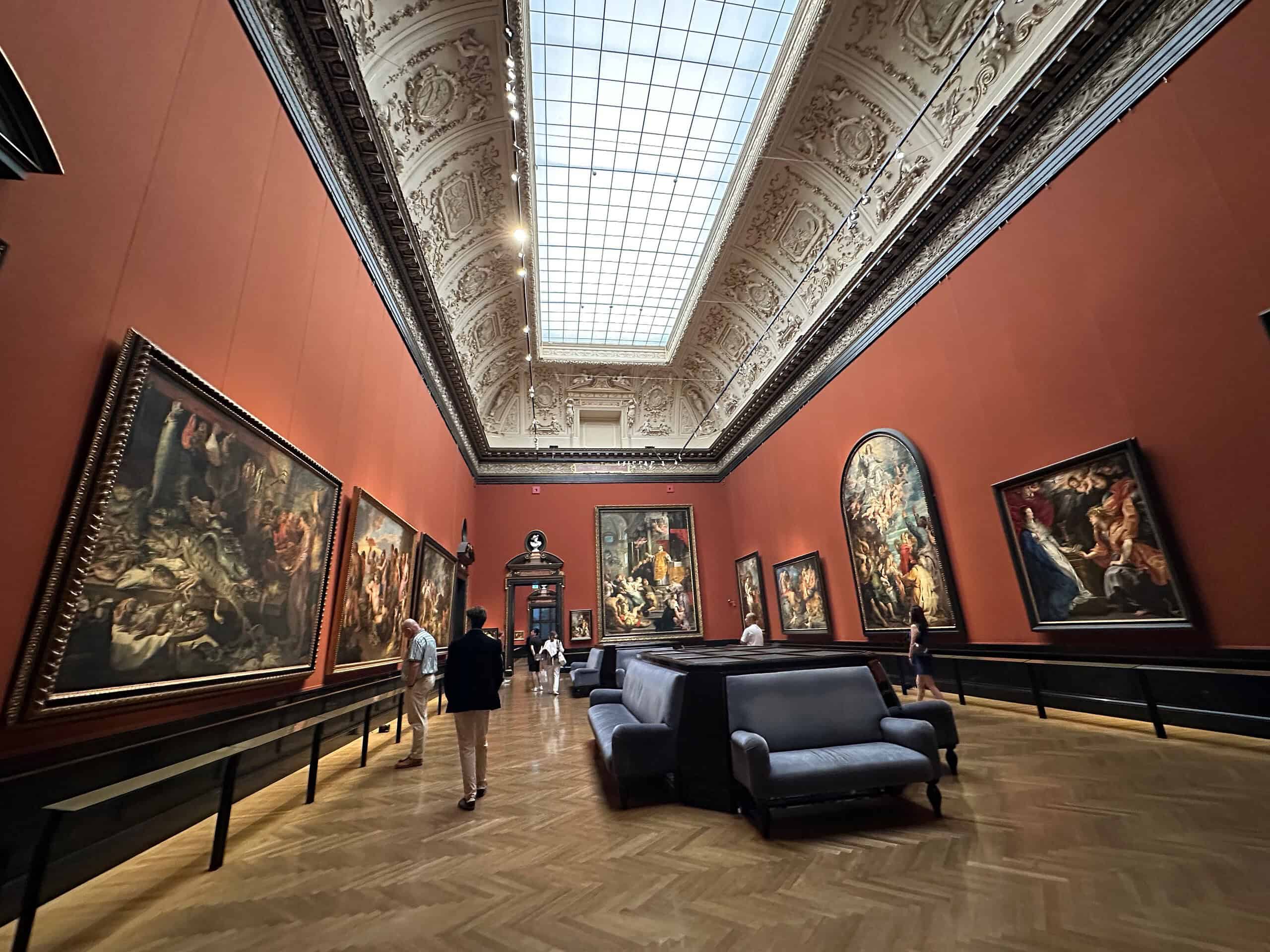 Visitors viewing paintings in a red-walled gallery at the Kunsthistorisches Museum in Vienna
