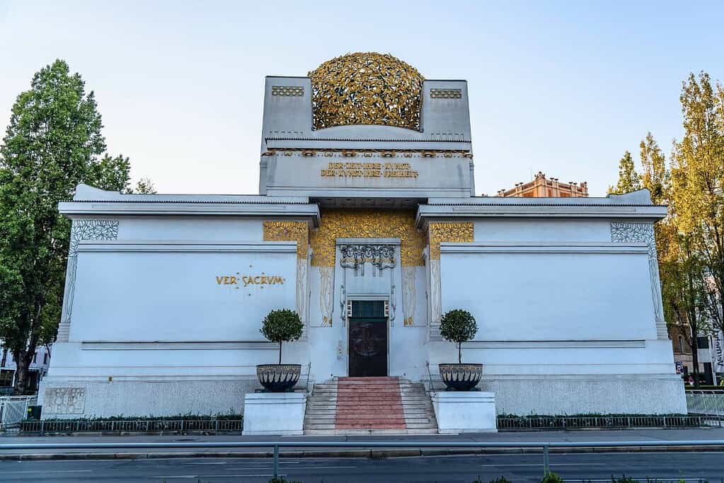 Front exterior of the Vienna Secession building, a white Art Nouveau structure with gilded ornament and a distinctive golden laurel-leaf dome, photographed from across the street in Vienna