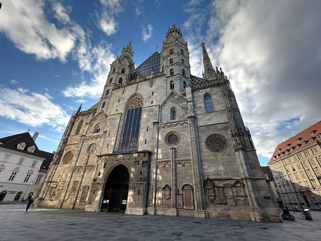 Exterior of St. Stephen’s Cathedral in Vienna, viewed from Stephansplatz beneath a blue sky with dramatic clouds