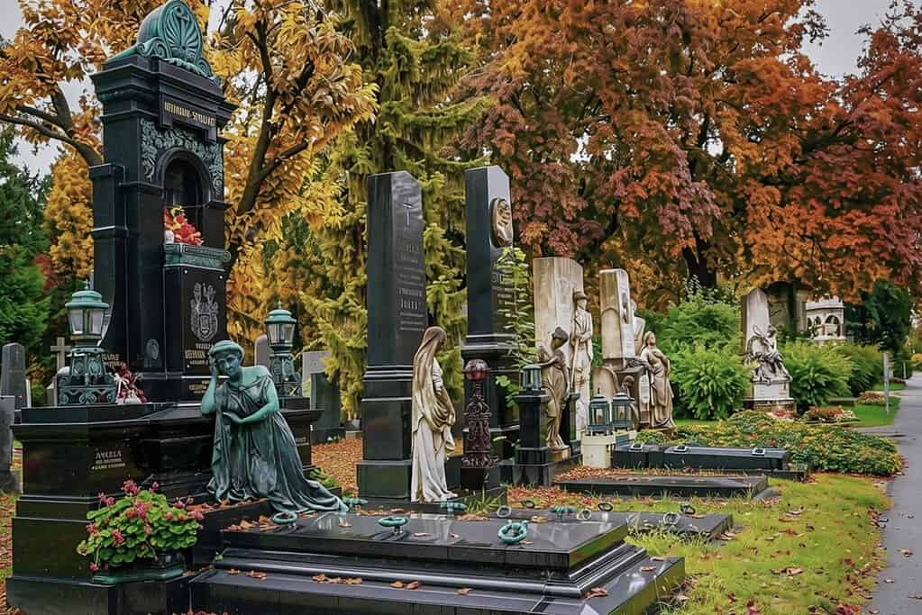 Statues and headstones at Vienna Central Cemetery with trees in autumn colors in the background