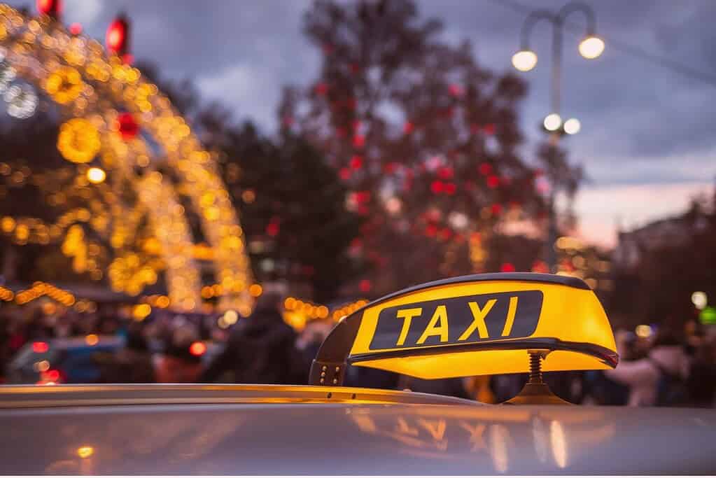 Taxi with its yellow rooftop light glowing in front of a Christmas Market in Vienna, Austria decorated with lights and a Christmas tree