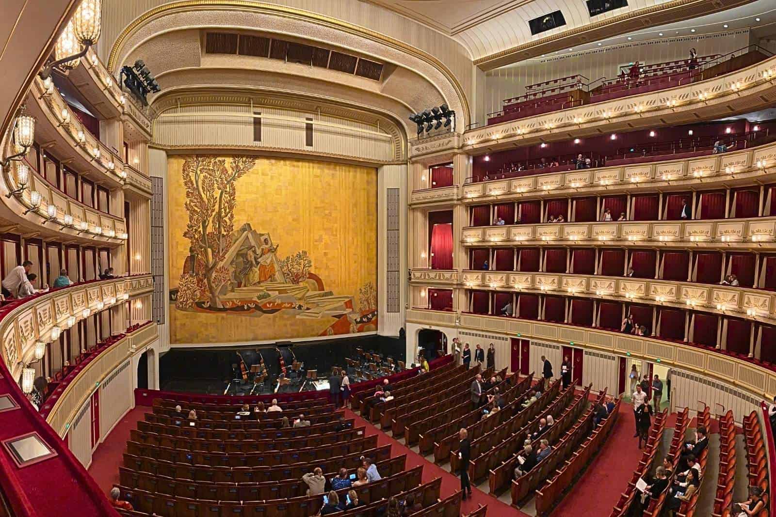 Interior of the Vienna State Opera auditorium, showing the stage, rows of seating, and multiple tiers of red-and-gold boxes